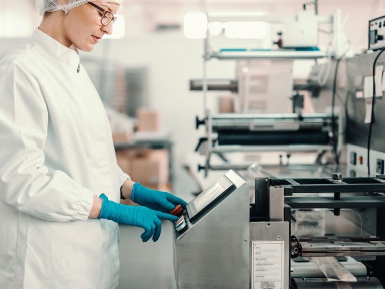 Young female employee in sterile uniform and blue rubber gloves turning on packing machine